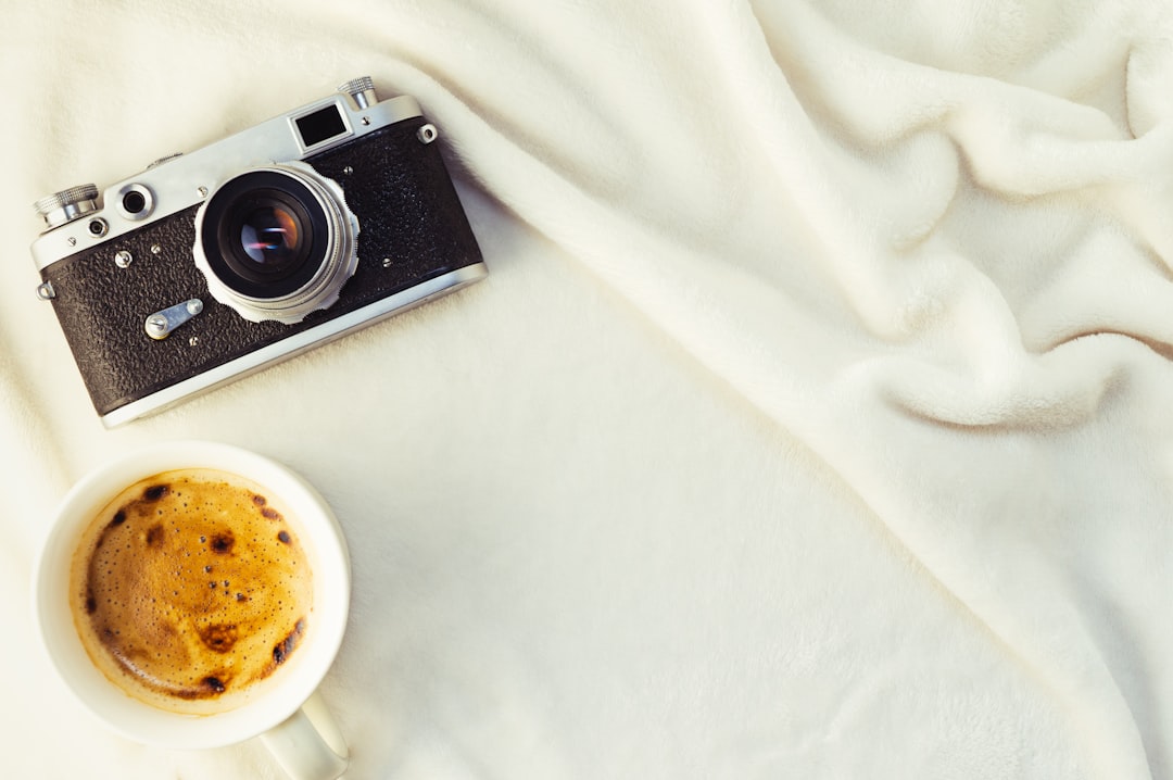 Photo de Konstantin Evdokimov appareil photo noir et argent à côté d'une tasse en céramique blanche sur un textile blanc